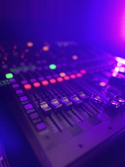 Gros plan sur les faders d'une console de mixage éclairée en violet