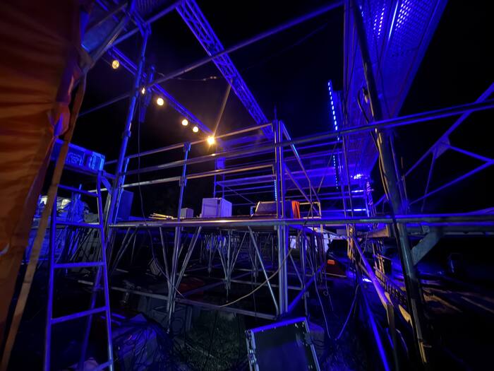 Structure de scène et gradins éclairés en bleu, montage avant le même festival de rock plein air